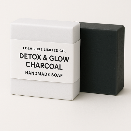 Black soap bar next to a white box labeled 'Detox & Glow Charcoal Handmade Soap' by Lola Luxe Limited Co. on a white background.