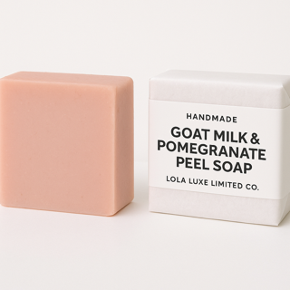 Bar of soap with a box labeled 'Handmade Goat Milk & Pomegranate Peel Soap' by Lola Luxe Limited Co on a white background.